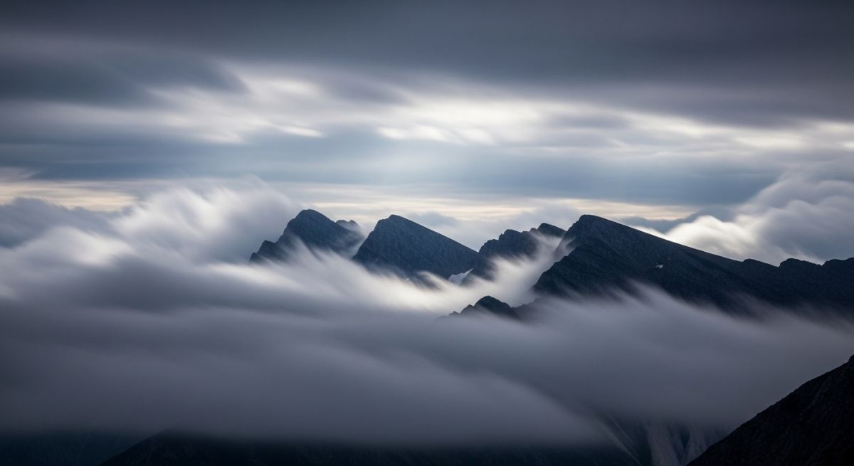 Wispy clouds moving across a dark mountain ridge.