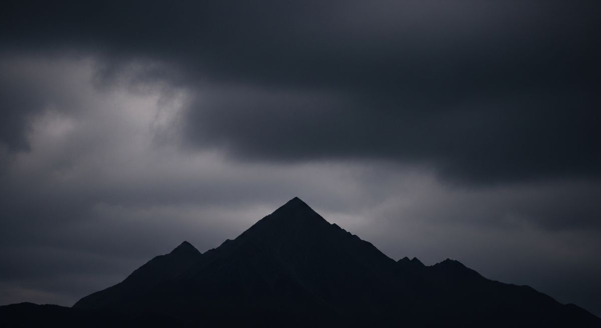 Minimalist silhouette of a dark mountain against a cloudy sky.